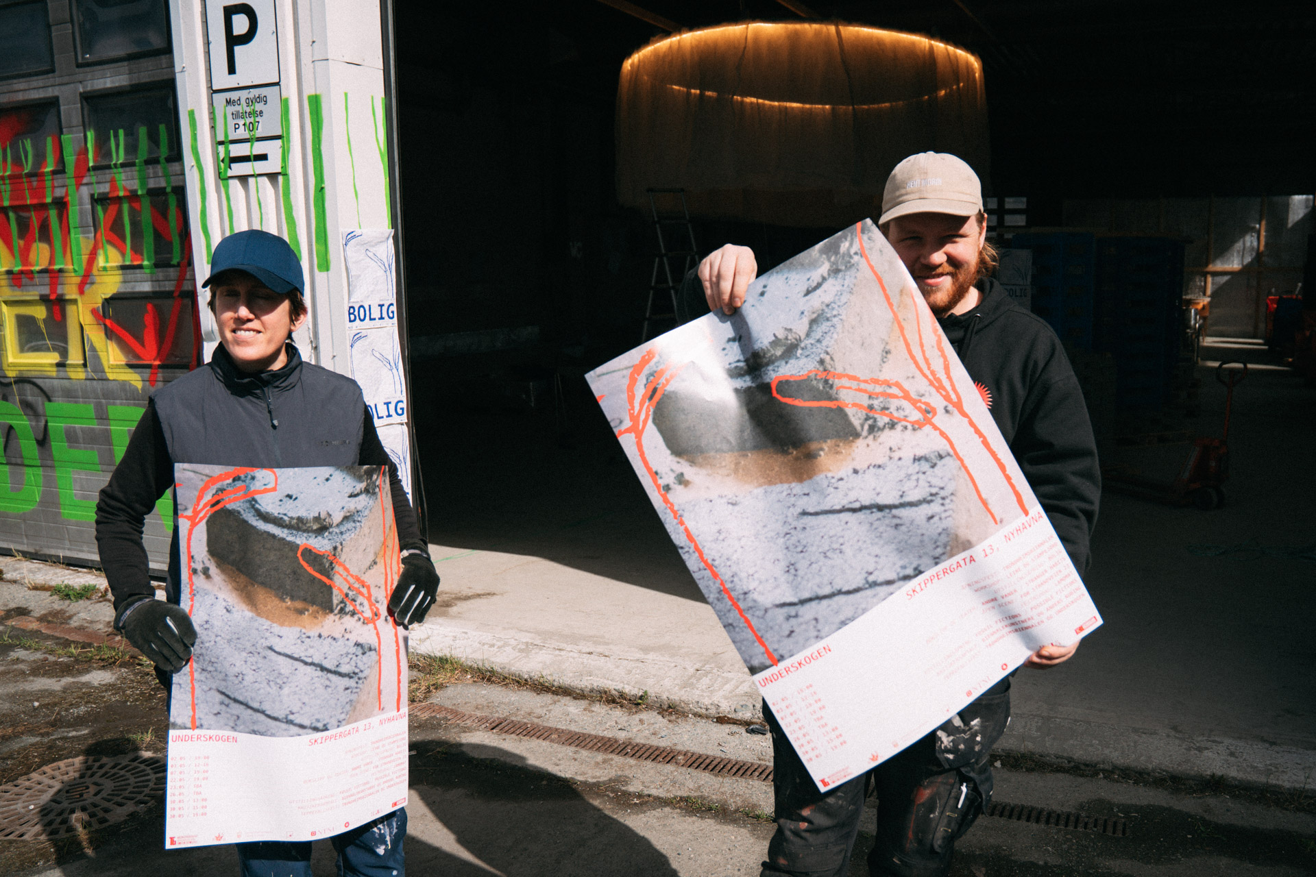 Johanna Gullberg og Are Bergerud står utenfor lageret på Nyhavna og holder hver sitt eksemplar av plakaten til utstillingen.