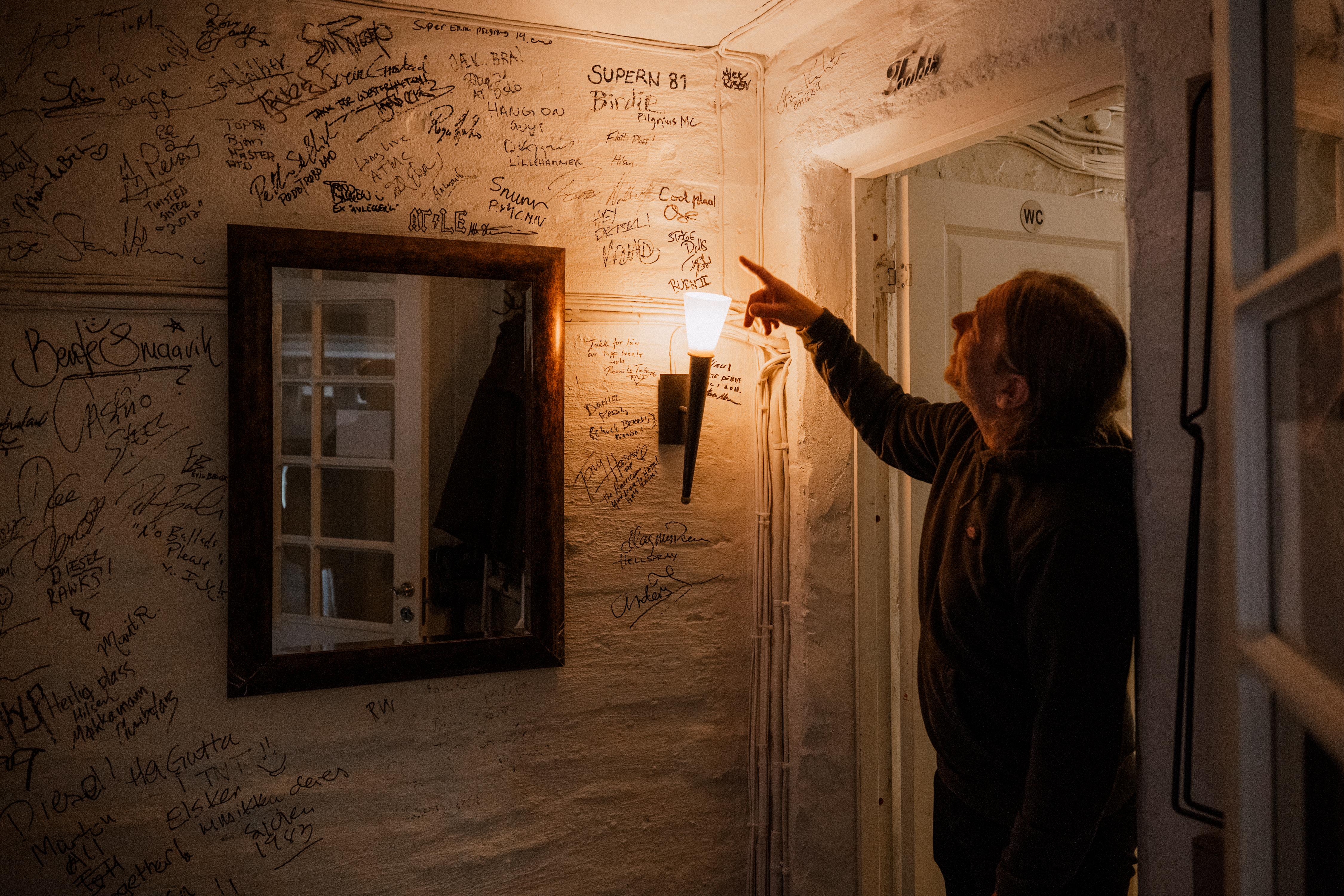 Stein-Roger Arnøy viser fram signaturer og hilsener på veggen i et lokale med lang musikkhistorie.